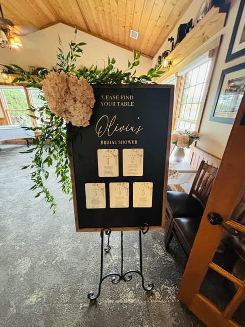 Black bridal shower seating chart displayed on an easel with blush hydrangeas and greenery