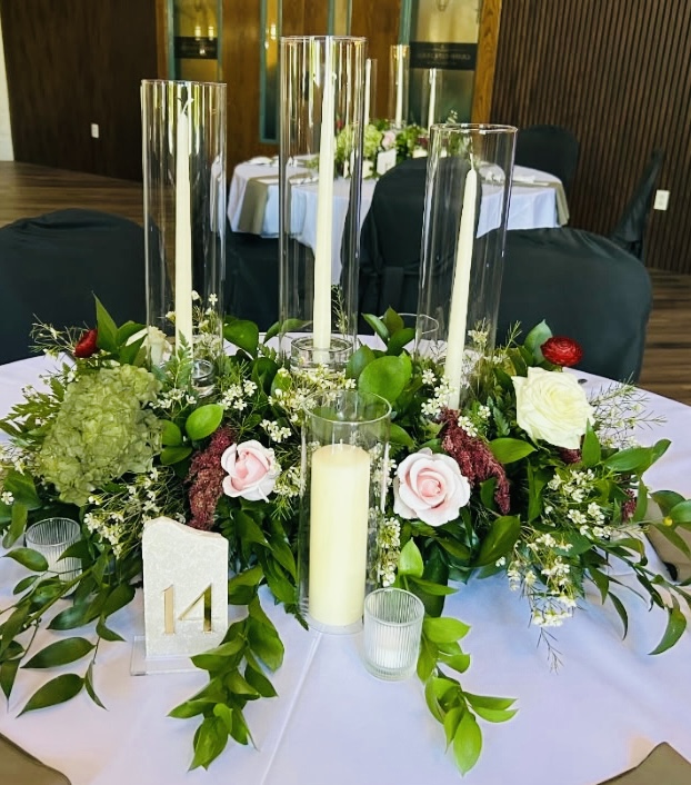 Wedding centerpiece styled with greenery, flowers, pillar candles, and glass cylinder vessels