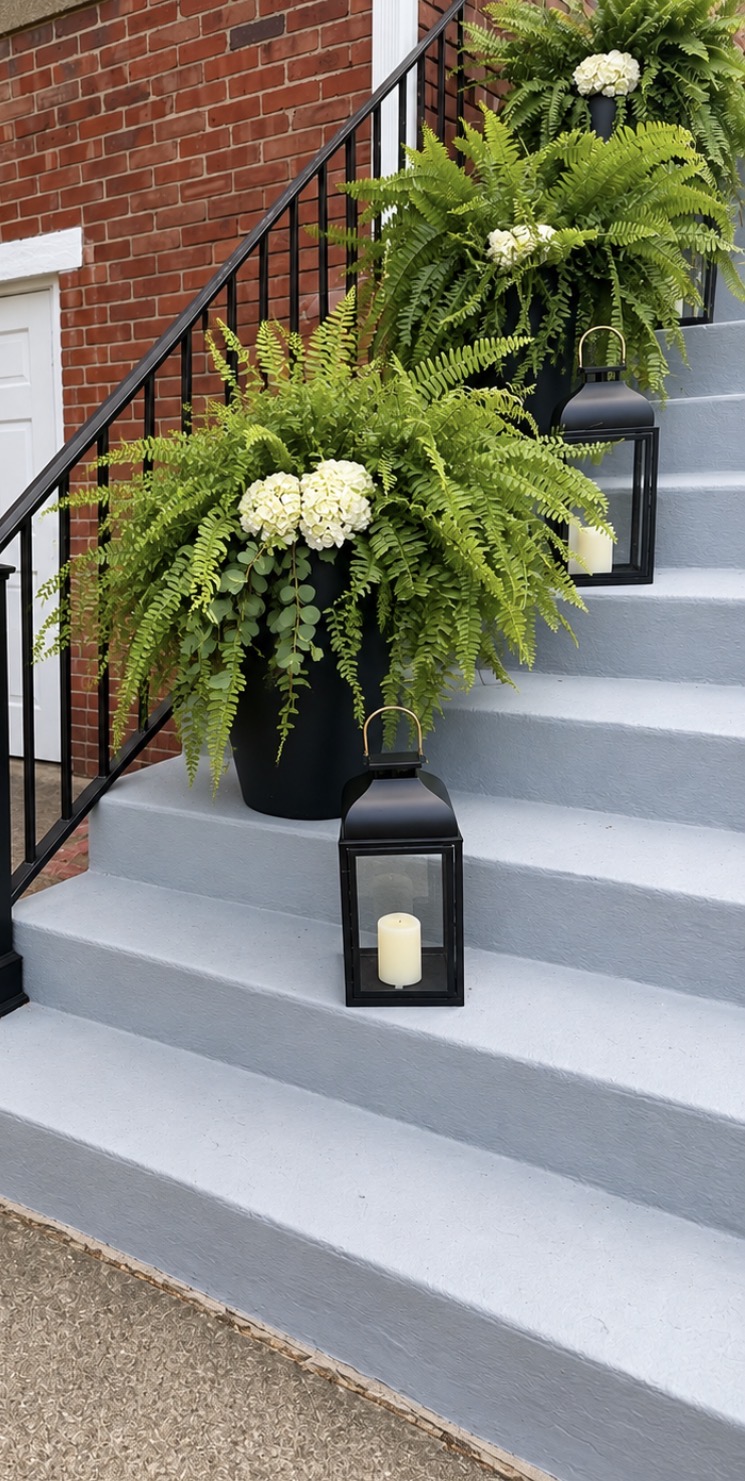 Church entrance steps decorated with full green and white floral planters and black lanterns