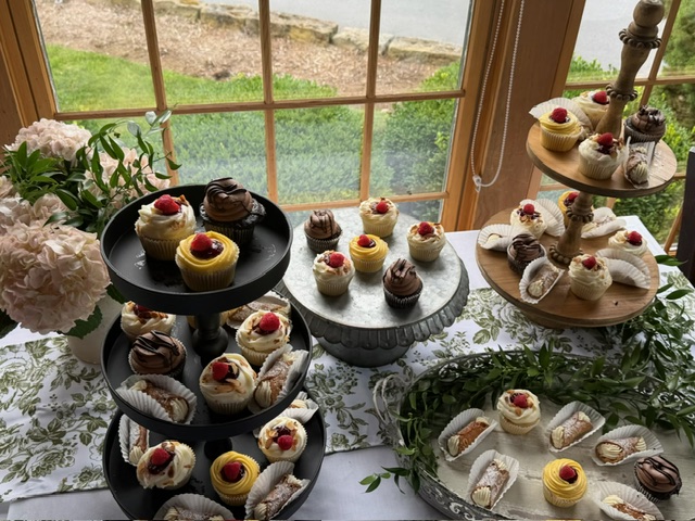 Assorted miniature desserts arranged on tiered stands beside hydrangeas and greenery