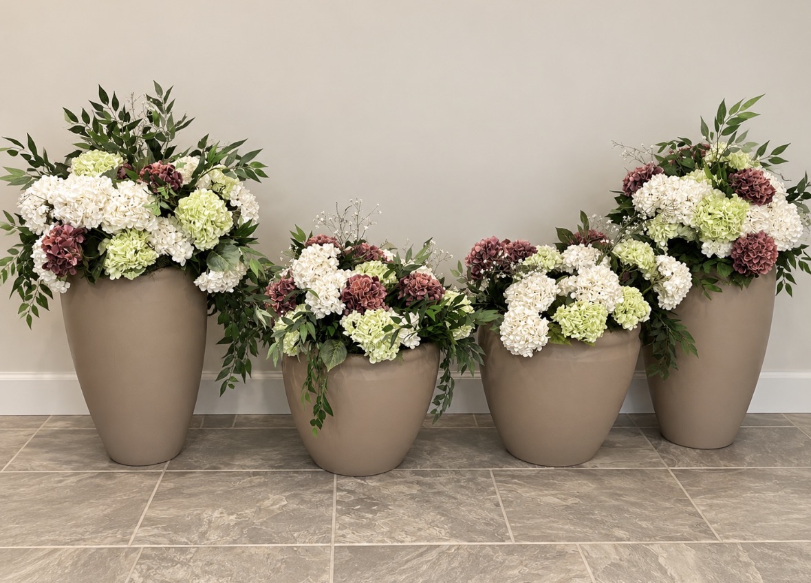 Collection of large taupe urns filled with white, blush, and burgundy flowers and greenery