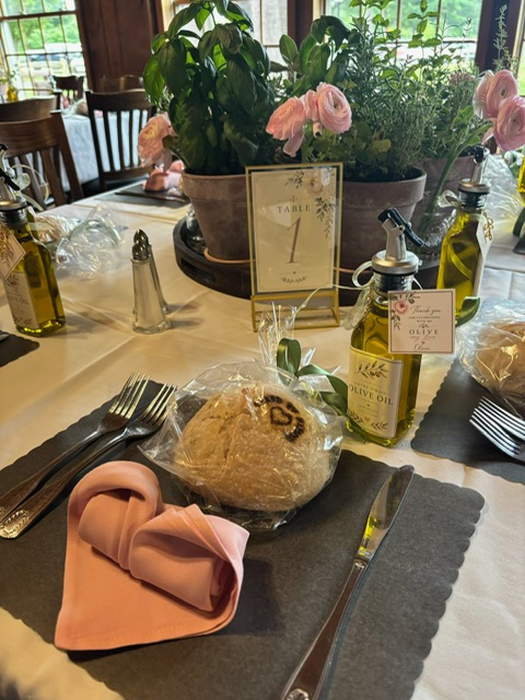 Garden-inspired place setting with blush napkin, favors, table number, and greenery